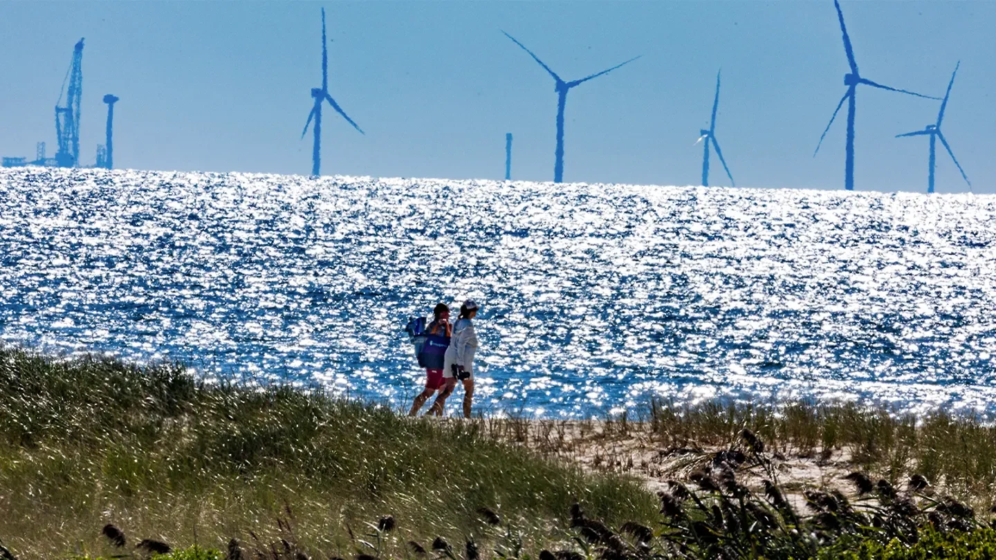 Madaket beachgoers walk along the beach in this 800mm telephoto view that compresses distance of the Vineyard Wind turbines 15 miles away.  (Stan Grossfeld/The Boston Globe via Getty Images)