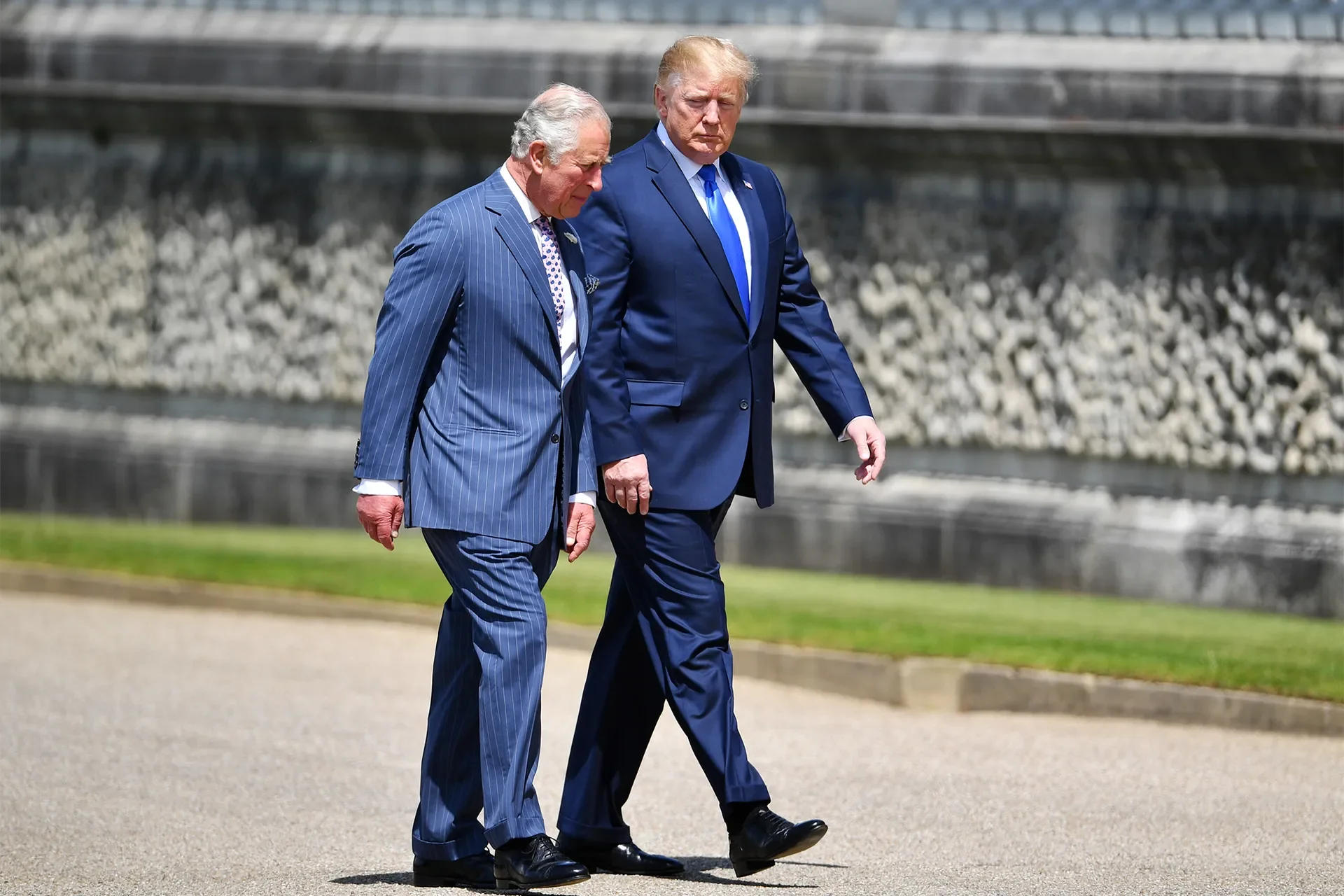 King Charles III and Donald Trump walk side-by-side outdoors on a sunny day