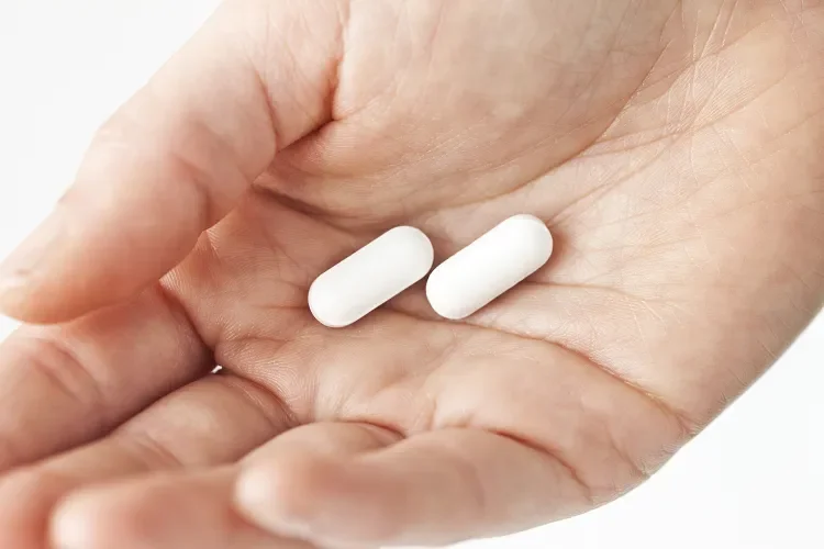 Stock image of a woman holding white pills. Credit : Getty