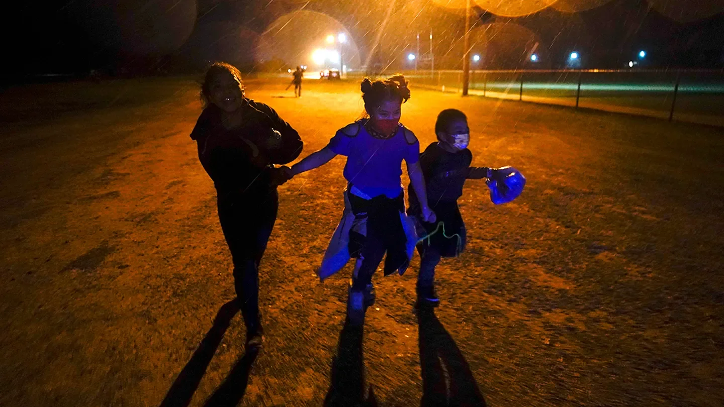 Young migrants hold hands as they run in the rain at an intake area after turning themselves in upon crossing the U.S.-Mexico border in Roma, Texas, May 11, 2021. (AP Photo/Gregory Bull)